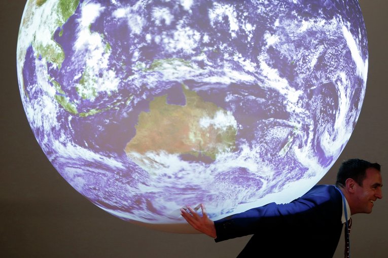 Участник позирует с репликой планеты на Всемирной конференции по изменению климата в Ле Бурже