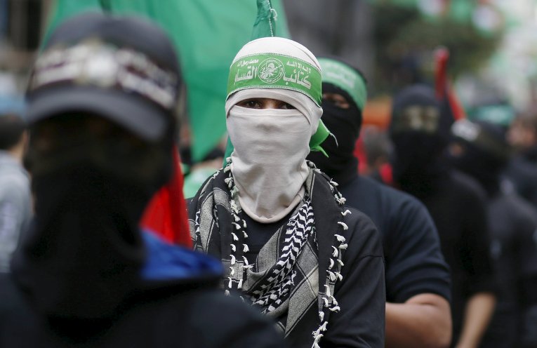 Палестинец в маске ХАМАС принимает участие в митинге по случаю 28-й годовщины основания ХАМАСа, в городе Газа