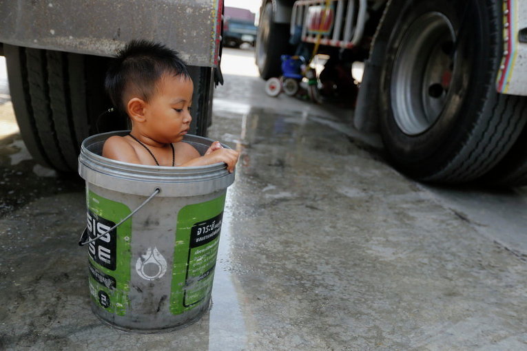 Мальчик купается в ведре рядом с грузовиком отца в центральной провинции Таиланда Чаинат