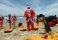 Индонезийские инструкторы серфинга, одетые как Санта-Клаусы, учат детей серфингу на пляже Кута на острове Бали, Индонезия