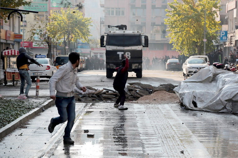 Протестующий бросает камни в полицейскую машину во время акции протеста против комендантского часа в юго-восточной части города Диярбакыр, Турция