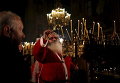 Человек, одетый как Санта-Клаус, зажигает свечу во время рождественской мессы в соборе Александра Невского в Софии, Болгария