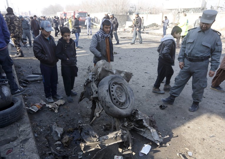 Афганский полицейский и местные жители смотрят на обломки автомобиля на месте теракта в Кабуле, Афганистан, 28 декабря 2015 г.