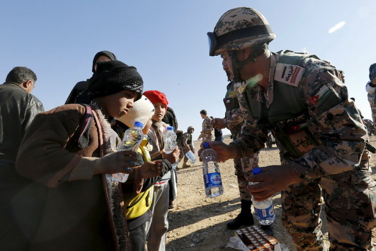 Иорданский солдат дает пищу и воду сирийским беженцам недалеко от города Рувайшед, к востоку от столице Аммане