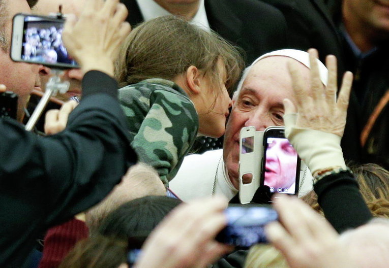 Ребенок целует Папу Франциска во время его прибытия на аудиенцию в зале Павла VI в Ватикане