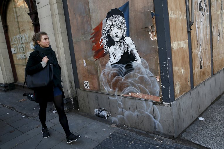 Женщина проходит мимо нового граффити напротив французского посольства в Лондоне. На фреске изображена мигрантка и слезоточивый газ, который, предположительно, использовался против мигрантов в лагере Кале