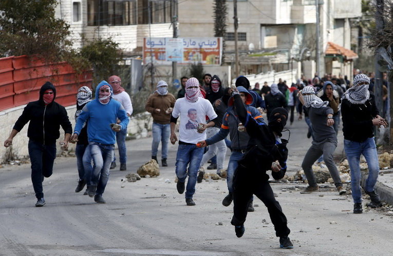 Палестинцы бросают камни в израильских военных в ходе столкновений в лагере беженцев к северу от города Хеврон