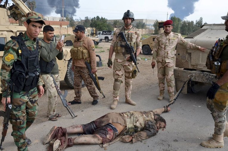 Бойцы иракских сил безопасности стоят над телом боевика Исламского государства, привязанного к задней части транспортного средства в районе Абу-Грейб, к западу от Багдада.