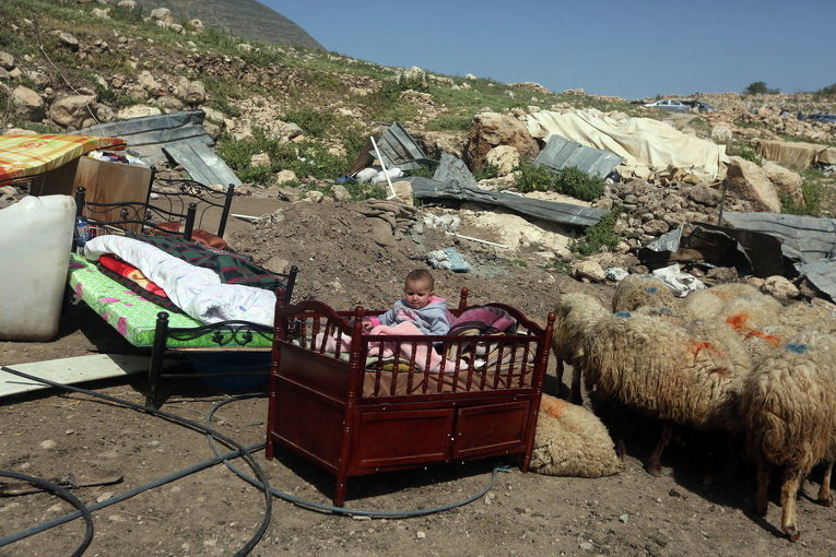 Палестинский ребенок сидит в своей кроватке возле своего дома, после того, как был разрушен бедуинский лагерь в Хирбет Тана к востоку от палестинского города Наблус