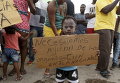 Африканский мальчик-мигрант на пограничном посту с Панамой держит плакат с надписью Нам нужна помощь от всемирной организации во время акции протеста в Пасо Каноас, Коста-Рика