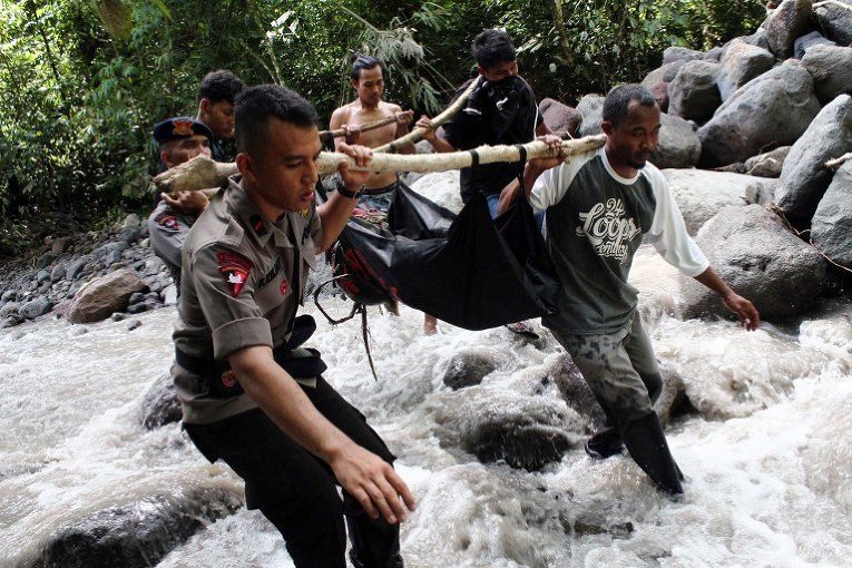 Индонезийские полицейские и местные жители несут тело жертвы наводнения на Северной Суматре