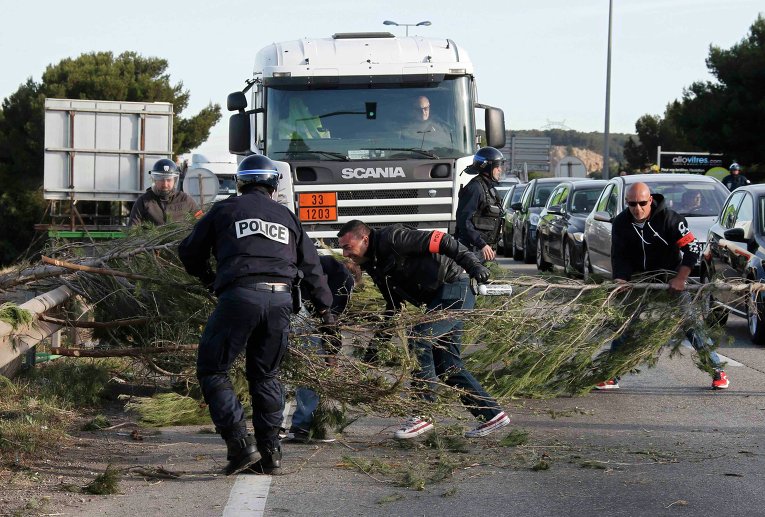 Французские жандармы убирают ветки деревьев, которые  в знак протеста положили на трассу бастующие рабочие нефтеперерабатывающего завода на Фос-сюр-Мер, близ Марселя, Франция.