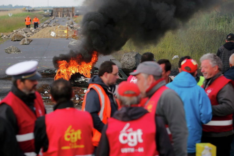 Протестующие работники профсоюзов стоят возле горящей баррикады, которая блокирует вход в топливное депо SFDM вблизи нефтеперерабатывающего завода Donges, Франция