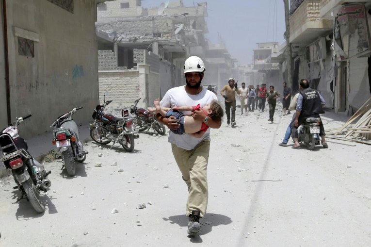 Член гражданской обороны несет девочку, раненную в результате авиаудара в сирийской провинции Идлиб