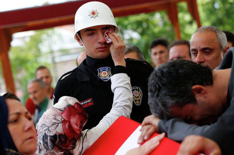 Женщина вытирает слезы члену почетного караула во время похор полицейских, которые погибли в результате теракта в Стамбуле