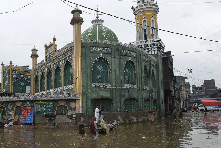 Пакистанские рабочие пробираются через поток воды после сильных дождей в Лахоре