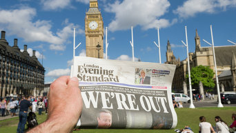 Мужчина держит в руке газету у здания парламента в Лондоне после референдума по сохранению членства Великобритании в Европейском Союзе.