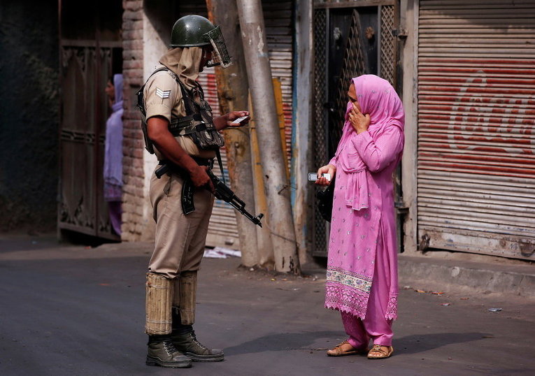 Индийский полицейский проверяет удостоверение личности женщины во время комендантского часа в Шринагаре
