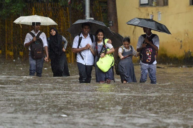 Индийские школьники идут по затопленной улице во время сильных ливней в Мумбае