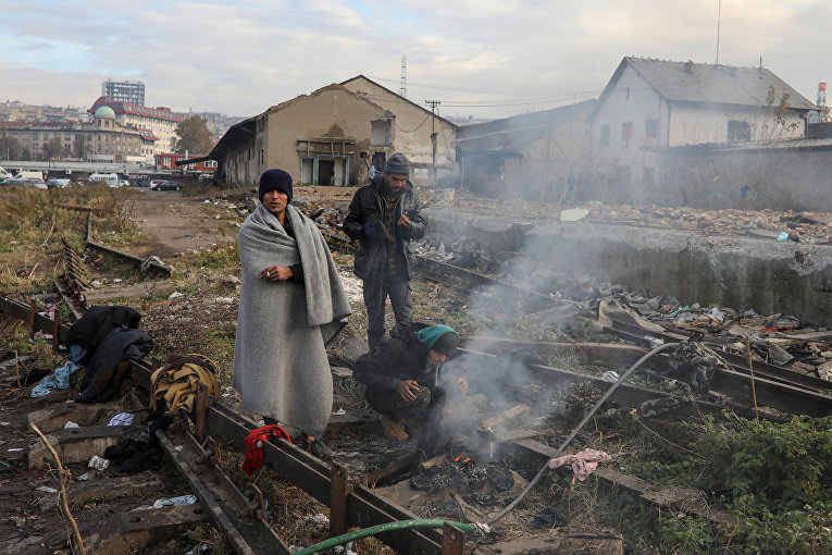 Нелегальные мигранты греются у костра на заброшенном складе в Белграде, Сербия