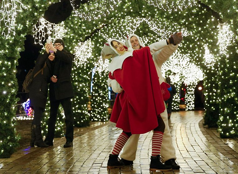 Уличные исполнители, одетые как рождественские эльфы, танцуют под праздничными украшениями в центре Киева