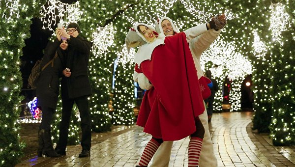 Уличные исполнители, одетые как рождественские эльфы, танцуют под праздничными украшениями в центре Киева