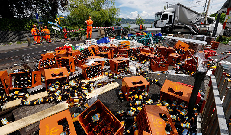 Спасатели стоят рядом с грузовиком, перевозящим напитки, который разбился на пригородном железнодорожном переезде в Хоргене, Швейцария