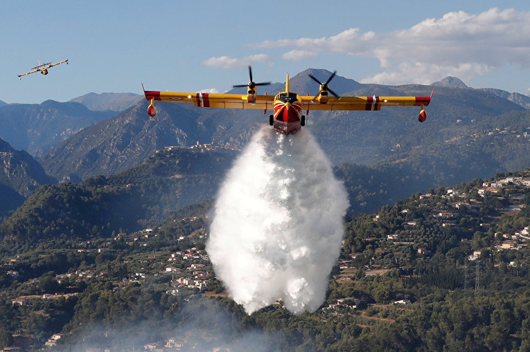 Канадский пожарный самолет бросает воду на лесной пожар, который сжигает лес