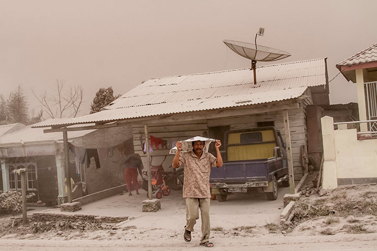 Житель деревни на северной Суматре закрывает голову от толстого полотна пепла после извержения вулкана.
