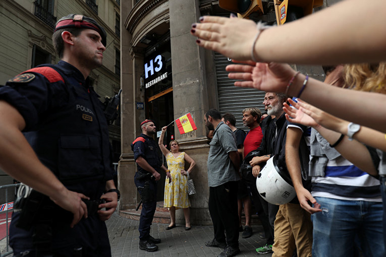 Женщина размахивает испанским флагом рядом с каталонскими региональными полицейскими и демонстрантами во время демонстрации через два дня после референдума о независимости Каталонии