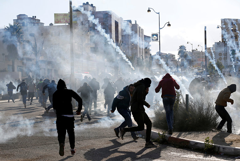 Палестинские протестующие бегут от слезоточивого газа, примененного израильскими войсками во время столкновений в знак протеста против решения президента США Дональда Трампа признать Иерусалим столицей Израиля, недалеко от еврейского поселения Бейт-Эль
