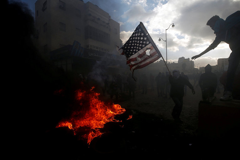 Палестинский протестующий готовится сжечь флаг США во время столкновений с израильскими войсками в знак протеста против решения президента США Дональда Трампа признать Иерусалим столицей Израиля, недалеко от еврейского поселения Бейт-Эль