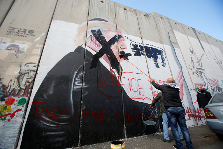 Палестинский человек перечеркивает стену, изображающую президента США Дональда Трампа, который нарисован на части израильского барьера, в городе Вифлеем на Западном берегу