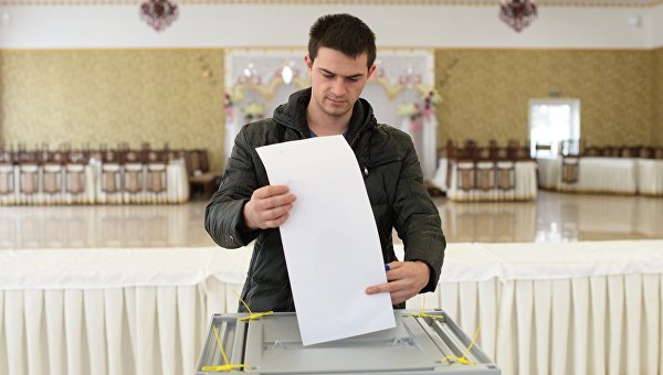 Молодой человек опускает бюллетень в урну на выборах президента РФ на избирательном участке в Бахчисарае