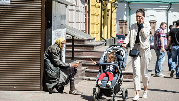 Молодая женщина с ребенком проходит мимо женщины, которая просит милостыню на центральной улице Киева