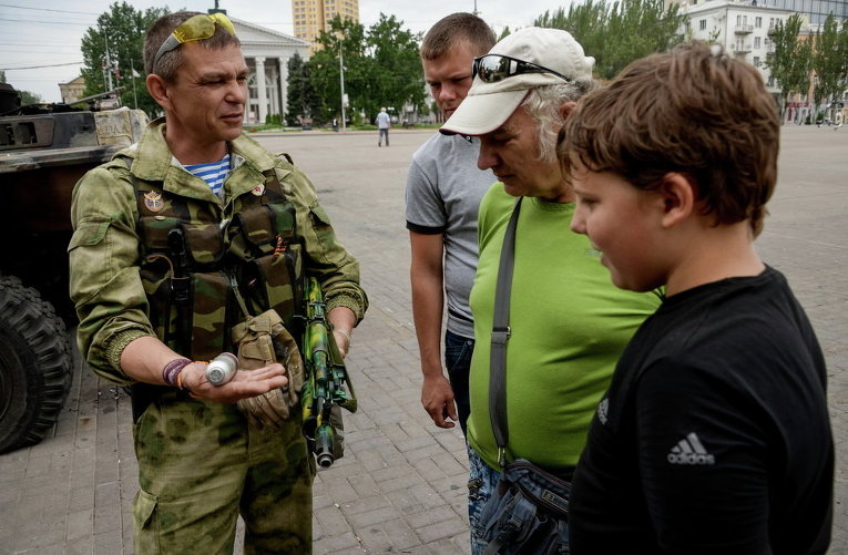 Ополченец показывает людям гранату во во время патрулирования площади Ленина в Донецке