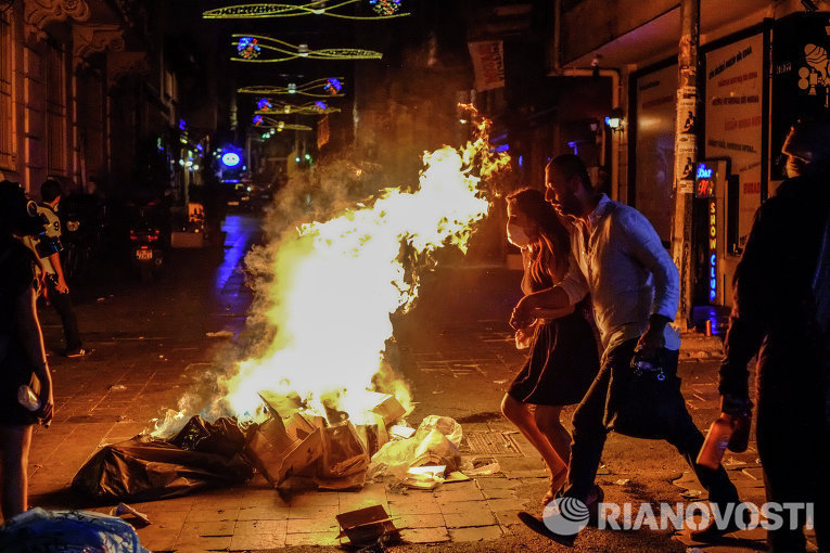 Прохожие идут мимо подожжённого мусора на улице Истикляль в Стамбуле