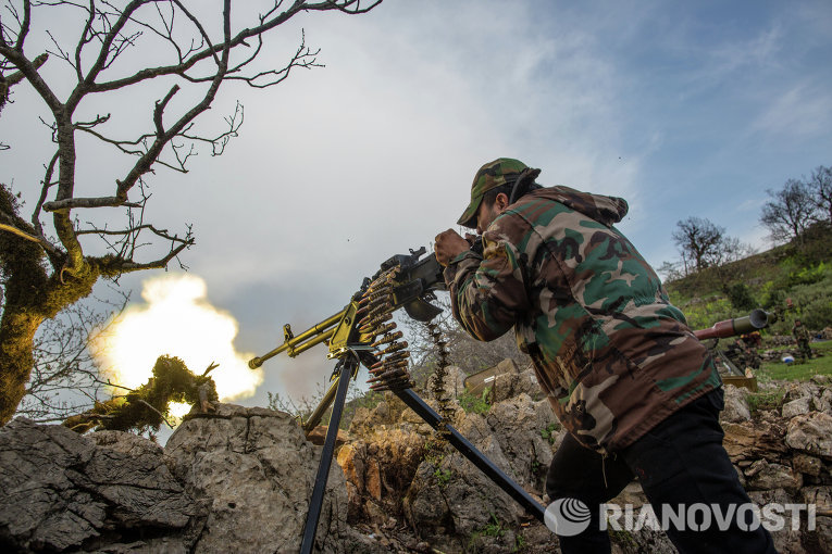 Военнослужащий правительственной армии Сирии ведет огонь из пулемета на позиции войск на одной из вершин возле города Кесаб, захваченного исламистами