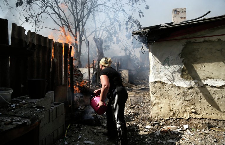 Местная жительница Донецка тушит пожар после обстрела