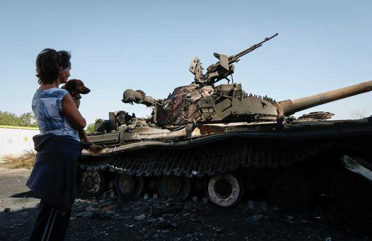 Местная жительница у сожженного украинского танка близ села Коминтерново в Донецкой области