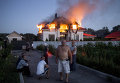 Жители соседних домов наблюдают за загоревшимся в результате авиаобстрела домом в поселке Николаевка неподалеку от Луганска.