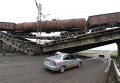 Автомобиль проезжает под взорванным железнодорожным мостом в районе Новобахмутовки и провисшим над ним грузовым составом.