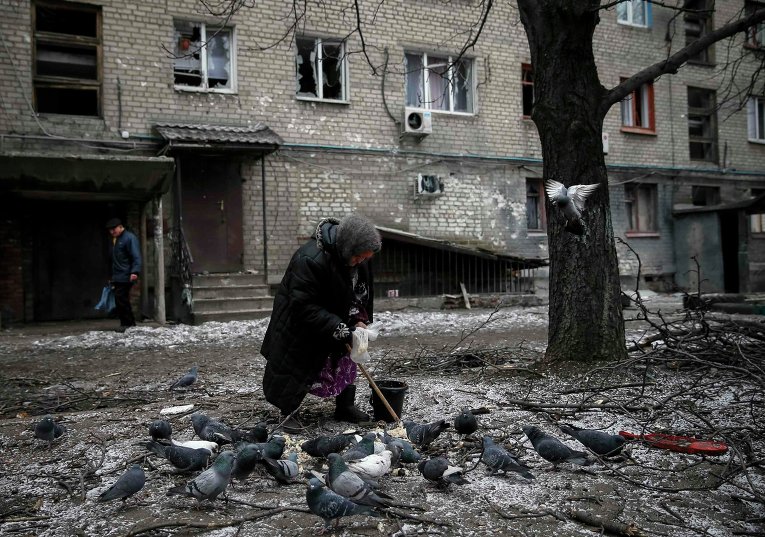 Пожилая женщина кормит голубей возле своего разрушенного дома в Дебальцево