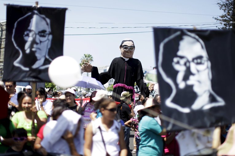 Демонстранты несут плакаты и фотографии покойного архиепископа Оскара Арнульфо Ромеро во время марша в честь 35-летия со дня его убийства в Сан-Сальвадоре