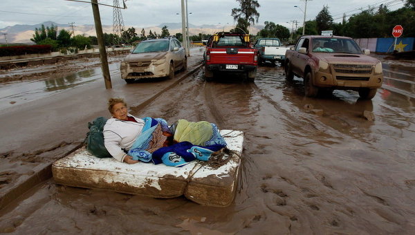 Женщина лежит на матраце на улице в грязи после ливней, которые вызвали сильные наводнения в Чили