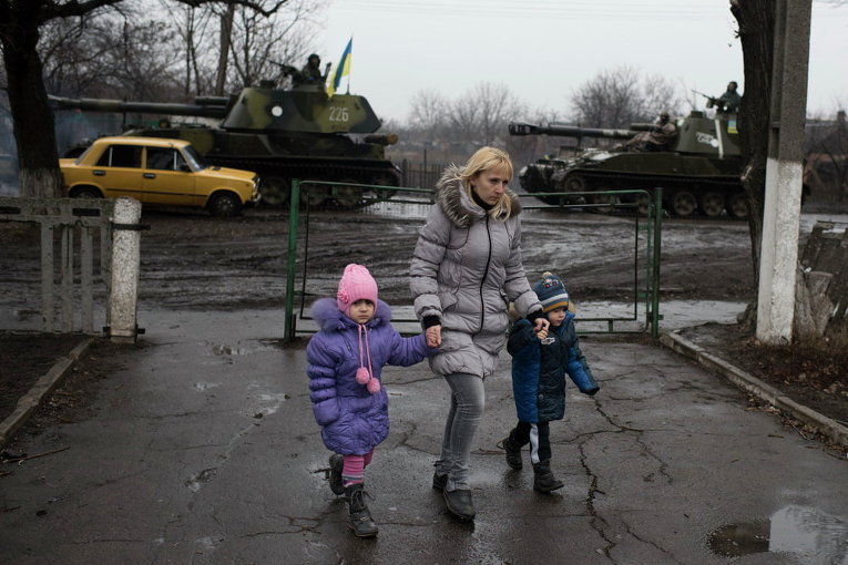 В Донецке местная жительница ведет детей в детский сад, позади нее - украинские военнослужащие на бронетехнике, 4 марта 2015 г