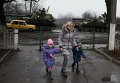 В Донецке местная жительница ведет детей в детский сад, позади нее - украинские военнослужащие на бронетехнике, 4 марта 2015 г