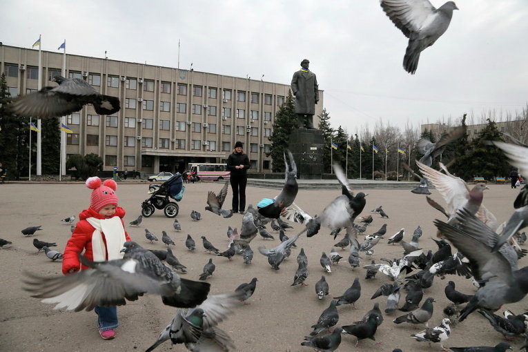 Ребенок играет с голубями на центральной площади Славянска, находящегося под контролем военных, 12 марта 2015 г