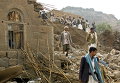 Йеменцы стоять среди развалин домов, разрушенных авиаударами в деревне недалеко от Саны