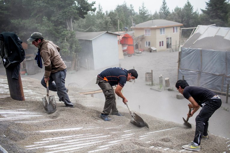 Мужчины удаляют золу с крыши здания после извержения вулкана Кальбуко в Чили